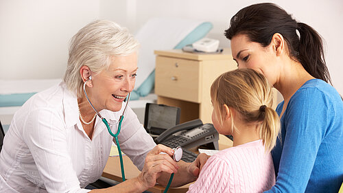 A mother holding a child whilst a GP checks on her using a stethoscope.